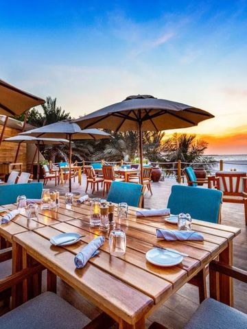 Freiluft-Restaurant mit Meerblick bei Sonnenuntergang, Holztische und Sonnenschirme