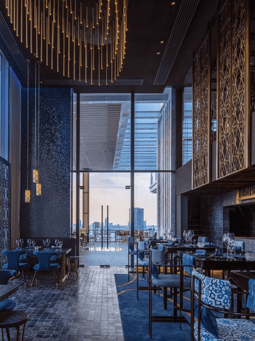 Das Restaurant der 137 Pillars Suite Bangkok besticht durch ein elegantes, modernes Interieur mit warmen Holztönen und stilvollen Details. Große Fenster lassen viel Tageslicht herein