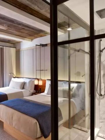 Moderne Hotelzimmer mit zwei Betten und stilvollem Bad mit glasierter Dusche.