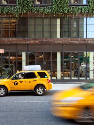 Fassade des Hotels mit grünem Bewuchs und vorbeifahrendem Taxi.