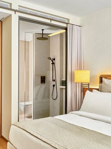 Helles Hotelzimmer mit Doppelbett und offener Dusche