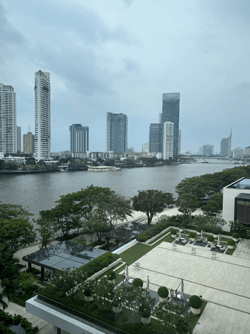 Durch die bodentiefen Fenster fällt der Blick auf den Chao Phraya River und die glitzernden Hochhäuser am gegenüberliegenden Ufer – eine eindrucksvolle Kulisse zwischen urbaner Energie und stiller Eleganz.