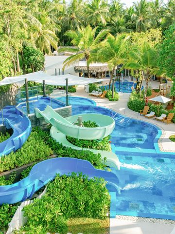 Poollandschaft mit Wasserrutschen umgeben von üppiger tropischer Vegetation.