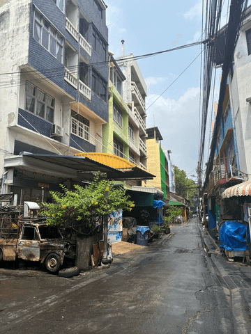 Eng verwobene, lebendige Gassen Bangkoks mit bunten Fassaden, Straßenständen und einem geschäftigen Treiben – ein typisches urbanes Flair voller Leben und Kontraste.