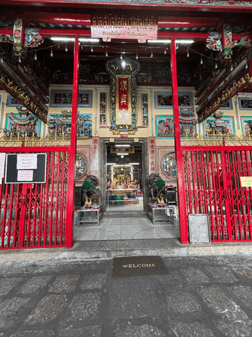 Ein reich verzierter Eingang mit roten Säulen, goldenen Schriftzeichen und kunstvollen Drachenornamenten markiert den Zugang zu einem chinesischen Tempel in Bangkok.