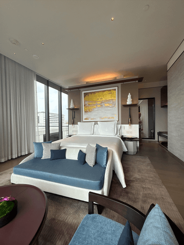 Ein elegantes Zimmer im Four Seasons Bangkok: Der stilvoll gestaltete Schlafbereich mit großzügigem Bett geht fließend in das luxuriöse Bad mit Glasfront über – modernes Design trifft auf zeitlose Ruhe.