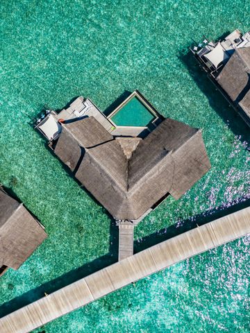 Luftaufnahme von Wasserbungalows auf Holzstegen über kristallklarem Wasser