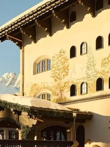 Hotel-Fassade mit dekorativen Wandmalereien und Alpenhintergrund