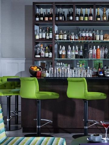 Elegante Hotelbar mit grünen Hockern und umfangreicher Spirituosenauswahl.