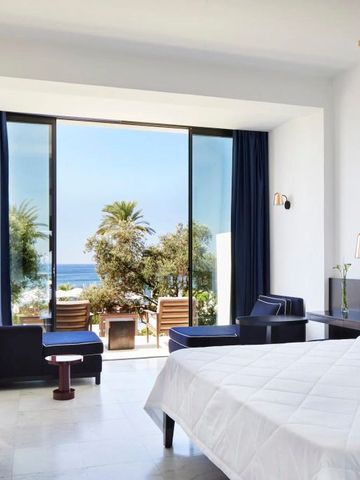 Geräumiges Zimmer mit großen Fenstern und Blick auf Palmen und Meer.