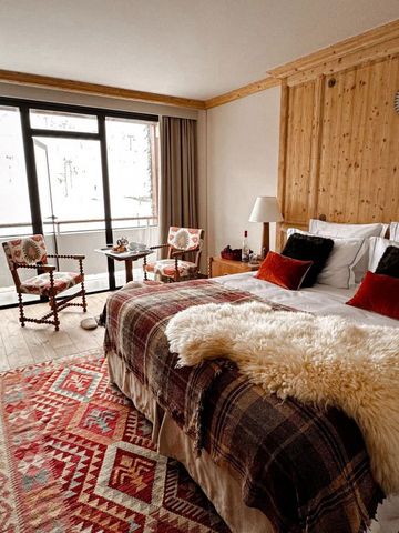 Gemütliches Hotelzimmer mit Holzdekor und flauschiger Wolldecke. Große Fenster mit Bergblick.