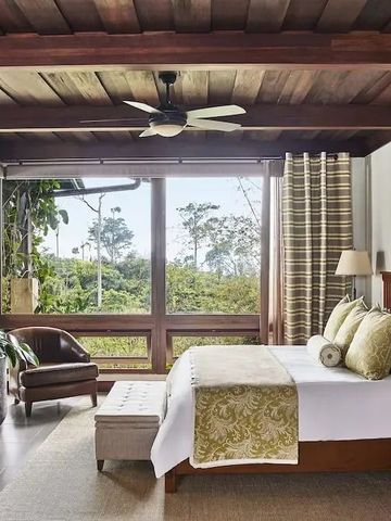 Helles Schlafzimmer mit großen Fenstern und Blick auf tropische Vegetation.