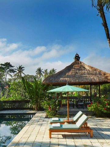 Sonnenschirme und Liegestühle am Pool mit exotischen Pflanzen und Pavillon im Hintergrund