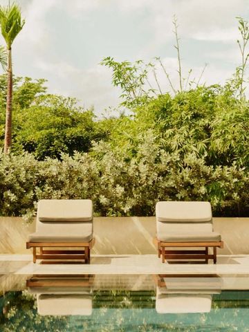 Sonnenliegen neben einem luxuriösen Pool von tropischen Pflanzen umgeben