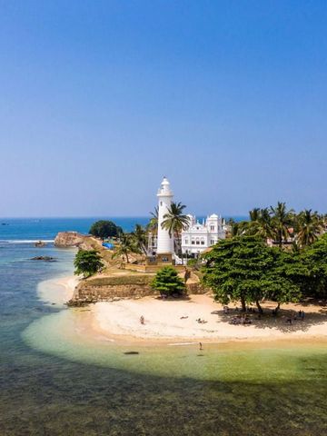 Leuchtturm an einem tropischen Strand mit Palmen und klarem Wasser