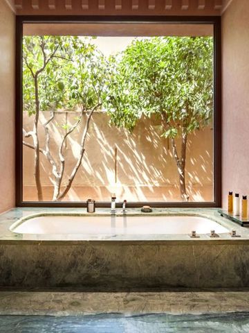 Geräumiges Badezimmer mit eingelassener Badewanne und Blick auf grüne Bäume.