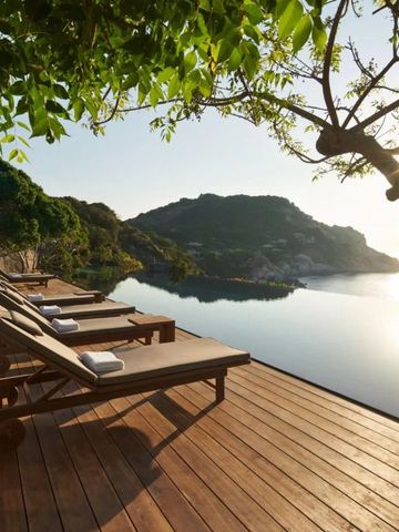 Sonnenliegen auf einer Holzterrasse mit Blick auf das Meer und bewaldete Hügel