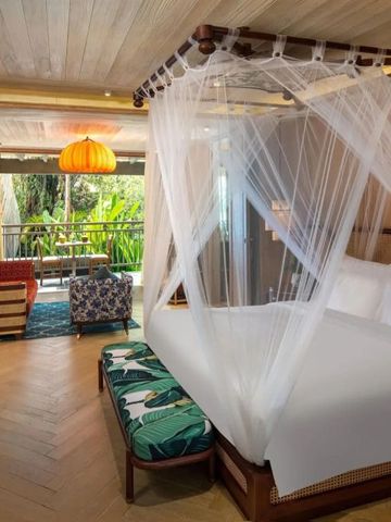 Geräumiges Luxushotelzimmer mit Himmelbett und exotischen Dekorationen sowie Balkonblick