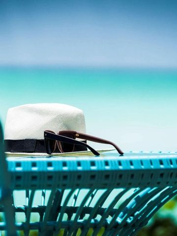 Hut und Sonnenbrille auf einem blauen Tisch mit Blick auf das Meer im Hintergrund