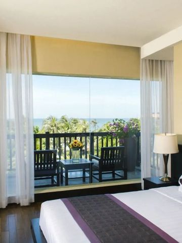 Hotelzimmer mit Doppelbett und großem Fenster mit Blick auf den Ozean und Balkon.