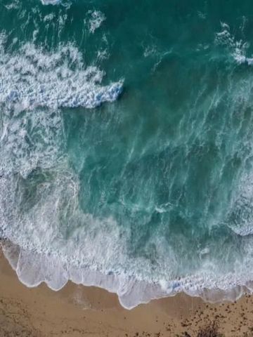 Luftaufnahme von Wellen, die auf einen Sandstrand treffen.