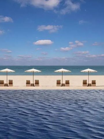 Infinity Pool mit Blick auf den Strand und das Meer bei klarem Himmel.