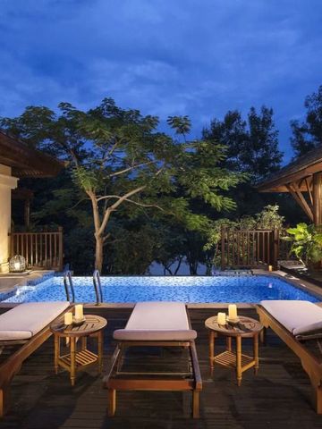 Beleuchteter Pool mit Liegen und tropischer Vegetation bei Dämmerung