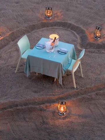 Romantisches Dinner-Setup im Sand mit Laternenbeleuchtung in Herzform angeordnet.