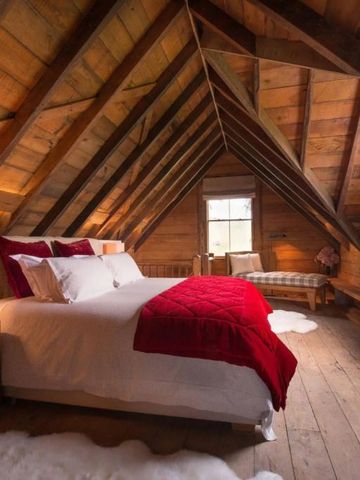 Rustikales Dachzimmer mit Holzbalken und roten Akzenten auf dem Bett.