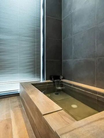 Holzbadewanne in modernem Bad mit großen Fliesen und natürlichem Licht.