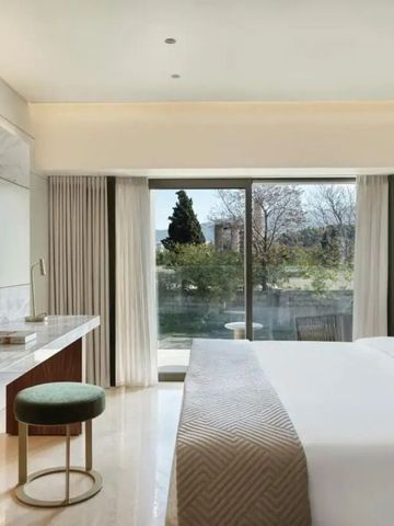 Helles Hotelzimmer mit großem Bett und Blick auf Bäume durch das Fenster