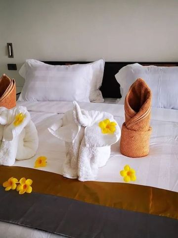 Detailaufnahme eines Hotelbettes mit kunstvoll gefalteten Handtüchern und Blütendekoration