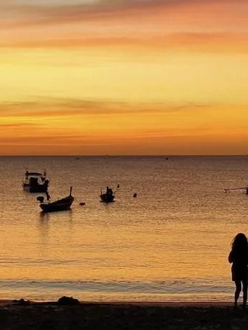 Sonnenuntergang am Strand mit Booten und silhouettierten Personen