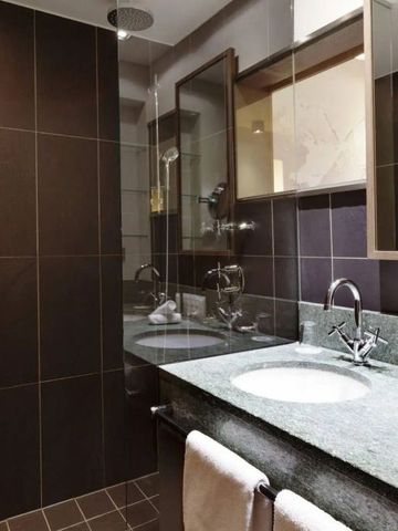 Modernes Badezimmer mit dunkel gefliesten Wänden, großem Spiegel und Waschbecken.