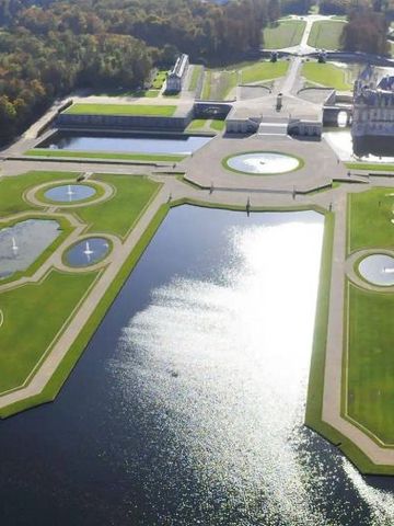 Luftaufnahme von symmetrisch angelegten Gärten und Wasserflächen am Schloss.