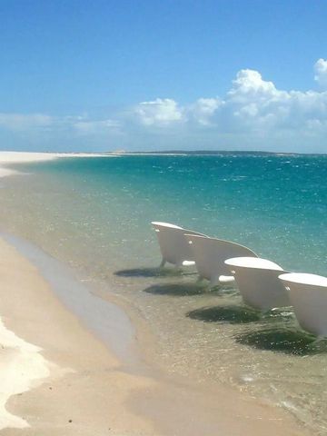 Weiße Liegestühle am Rande des türkisfarbenen Wassers auf einem feinen Sandstrand