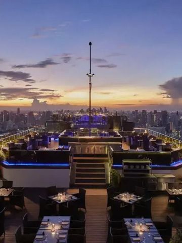 Stilvolle Rooftop-Bar mit atemberaubender Aussicht auf Bangkoks Skyline bei Sonnenuntergang.