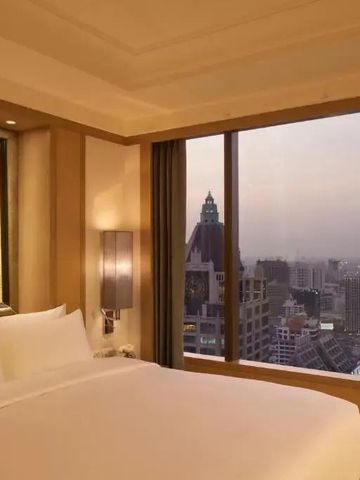 Elegantes Zimmer mit großen Fenstern und Blick auf Bangkoks Skyline bei Dämmerung.