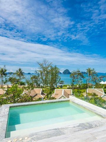Infinity-Pool mit Blick über tropische Dächer auf das Meer unter blauem Himmel