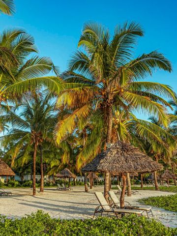 Traumhafter Strand mit Palmen und Strohschirmen bei klarem, blauem Himmel.