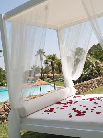 Romantische Liege mit roten Rosenblättern und Blick auf den Pool.