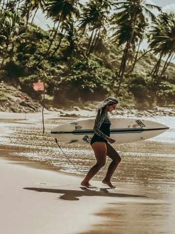 Frau mit Surfbrett am Strand mit Palmen im Hintergrund
