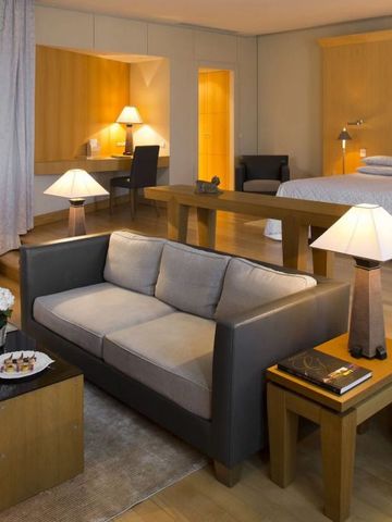 Elegante Suite mit Wohnzimmerbereich und Doppelbett. Holzelemente und warme Beleuchtung.