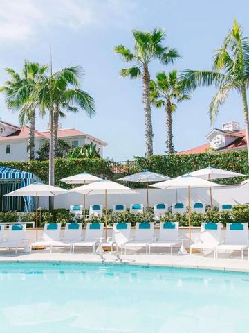 Liegen und Sonnenschirme am Pool mit Palmen und weißen Gebäuden