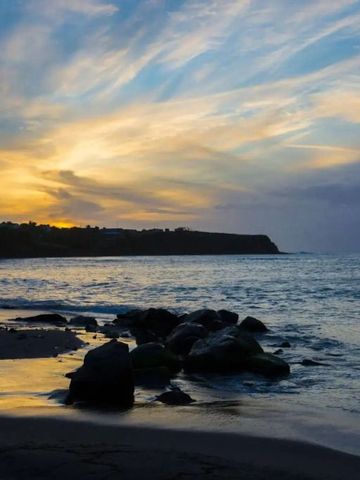 Dramatischer Sonnenuntergang über dem Meer mit Felsen am Strand