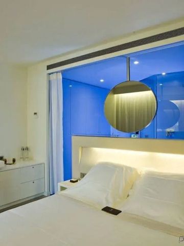 Modernes Zimmer mit Doppelbett und blauer Akzentwand im Badezimmer