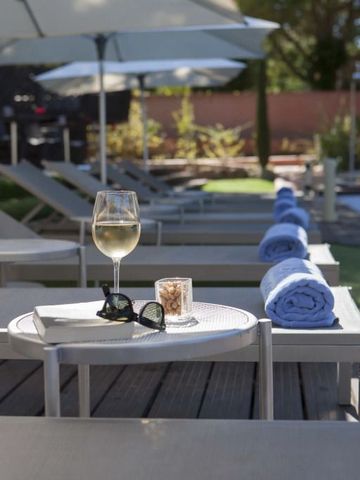 Weinglas und Sonnenbrille auf Tisch neben Poolliegen