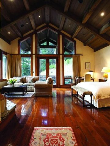 Luxuriöses Schlafzimmer mit Holzböden und großen Fenstern mit Blick ins Grüne