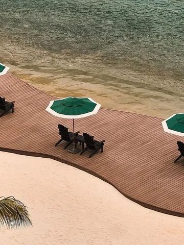 Holzdeck am Strand mit grünen Sonnenschirmen und Liegestühlen am Wasser