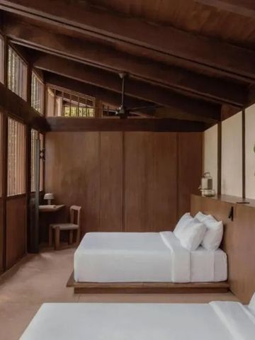 Zimmer mit hohen Holzdecken, zwei Betten und großen Fenstern mit Ausblick ins Grüne.